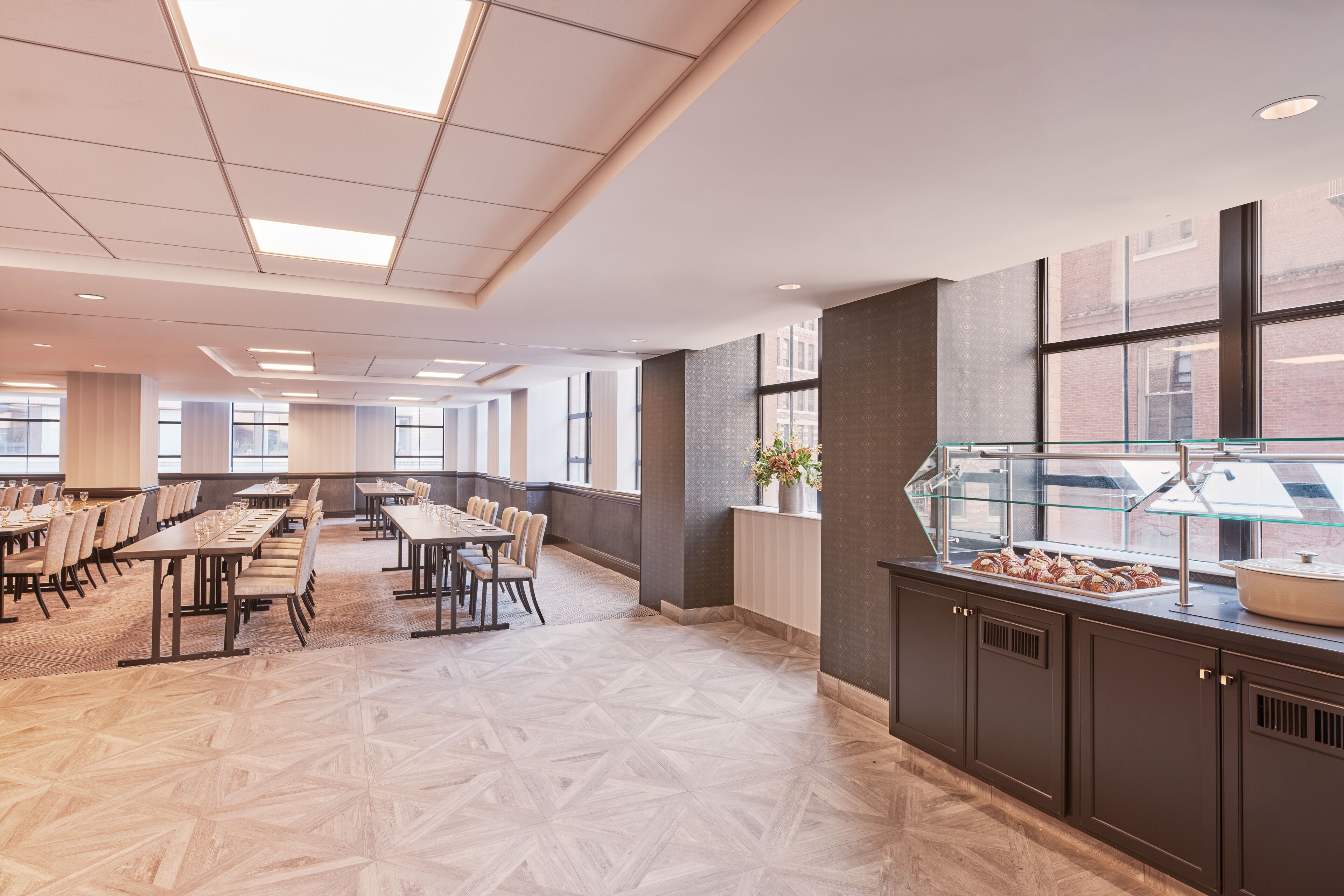 A spacious dining area with long tables and chairs, a buffet station, and large windows providing natural light.