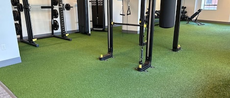 Un gimnasio con equipamiento de levantamiento de pesas, un saco de boxeo y una banca.