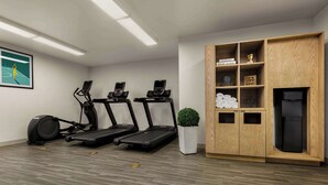 Une salle de sport équipée de tapis de course, d’un vélo elliptique et d’un vélo d’appartement. On y trouve également un meuble en bois avec des étagères, une horloge et une petite plante.