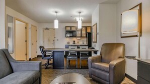 Une chambre d’hôtel moderne dotée d’un coin repas, d’une cuisine et d’un espace salon avec des fauteuils en cuir.