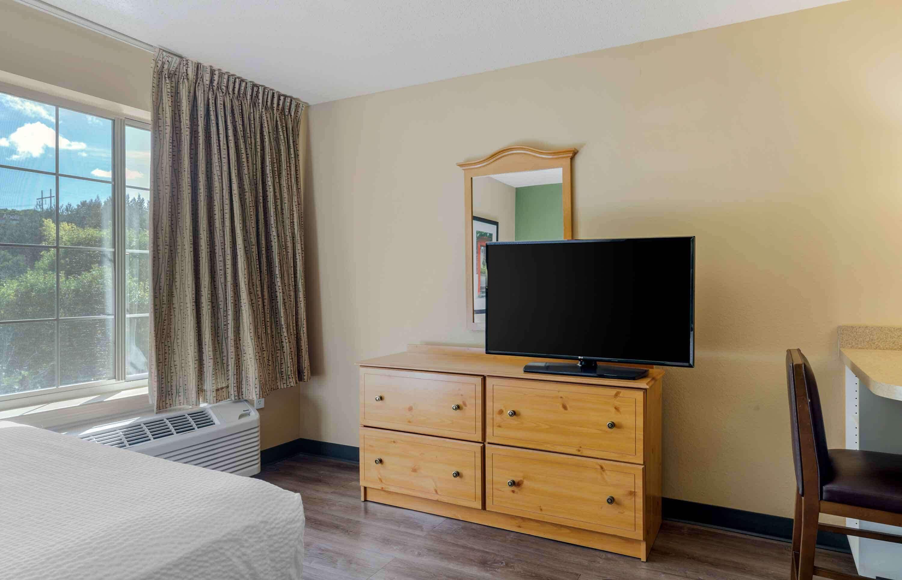 A hotel room with a bed, a TV on a wooden dresser, a chair, and a window with curtains.