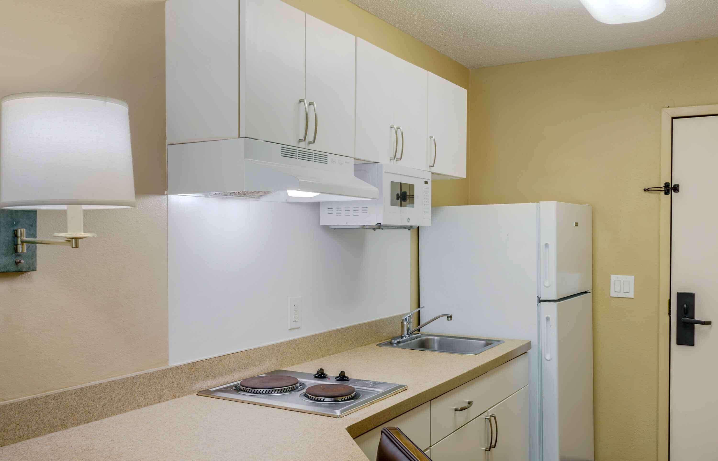 A compact kitchen with white cabinets, a built-in microwave, a stove, and a refrigerator.