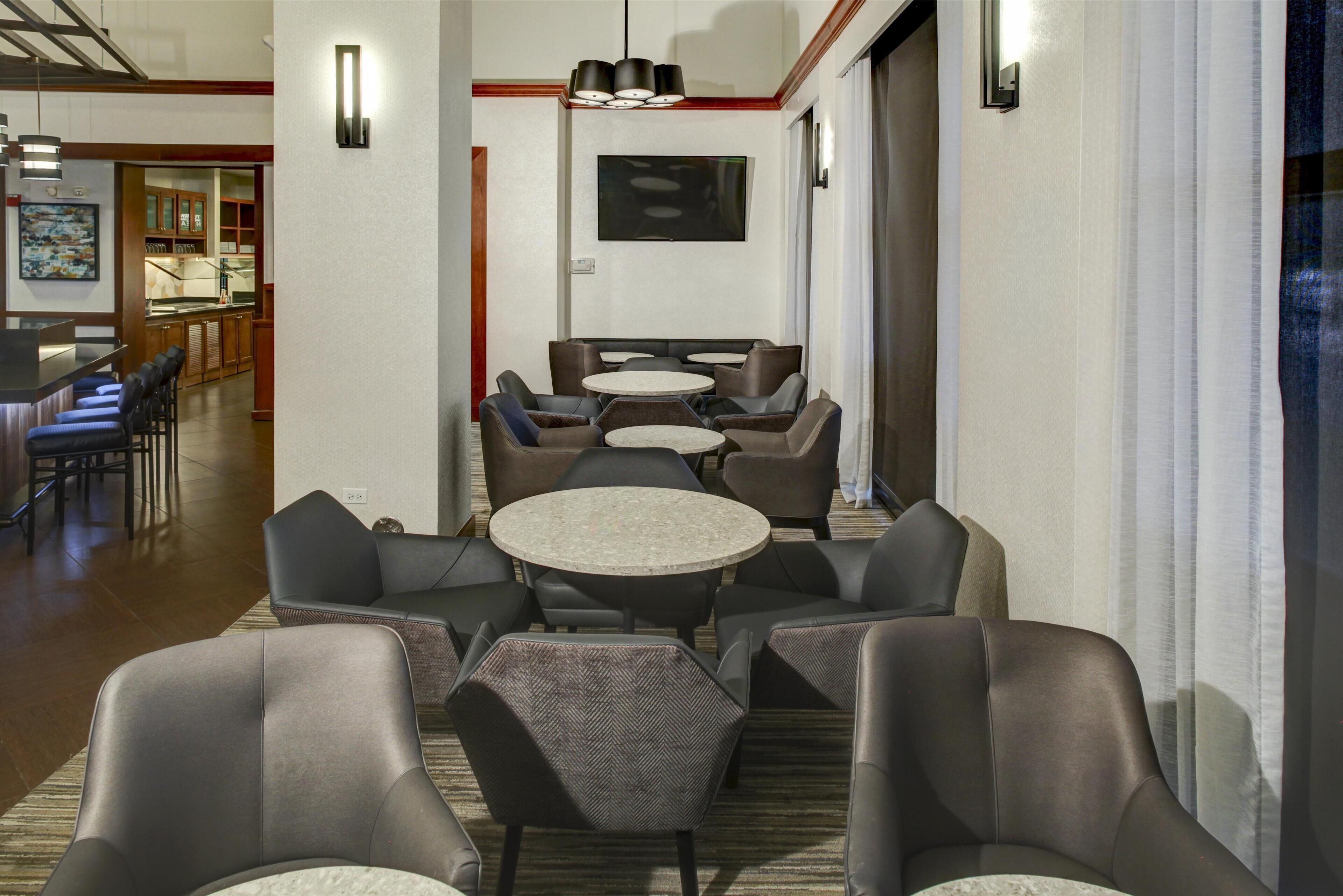 A hotel lobby with multiple seating areas, a bar, and a television mounted on the wall.