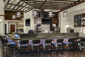 A modern bar area with a long counter, multiple bar stools, and overhead lighting. - Hyatt Place Detroit/Livonia (Livonia)