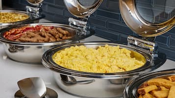 A buffet with various food items in stainless steel containers, including scrambled eggs, bacon, and fried potatoes.