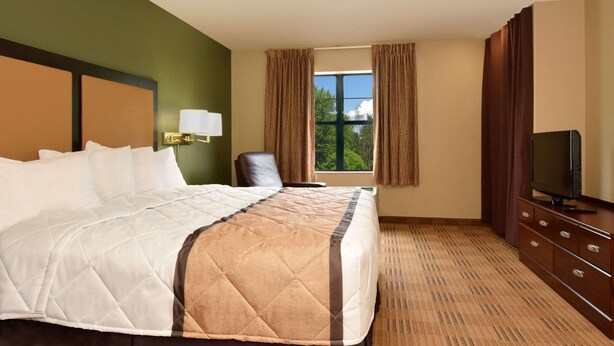 Una habitación de hotel con una cama grande, un televisor, una silla y una ventana con cortinas.