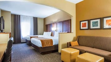 A hotel room with two beds, a sofa, a TV, and a carpeted floor.