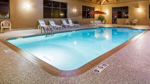Piscina interior con sillones reclinables y una mesa con sombrillas.