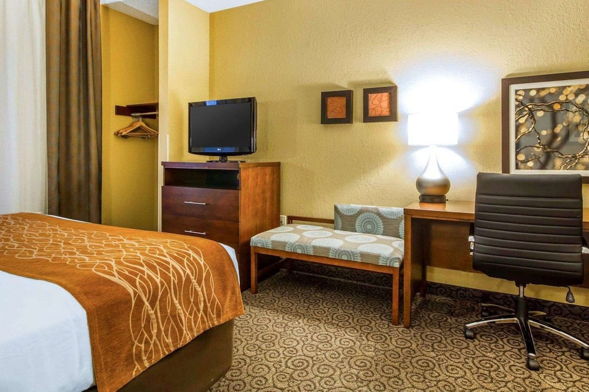 A hotel room with a bed, a desk with a chair, a television, a lamp, and a small table with a chair.