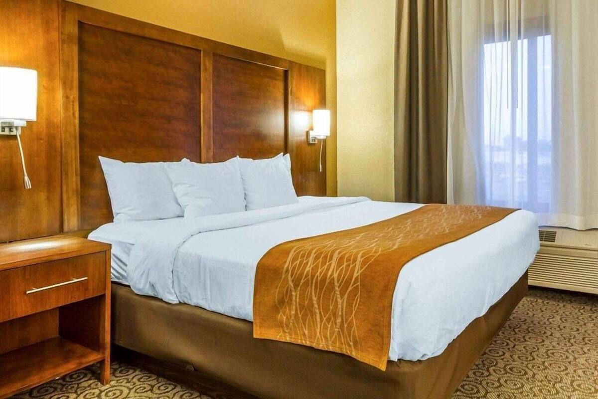 A hotel room with a large bed, wooden headboard, bedside table, and a window with curtains.