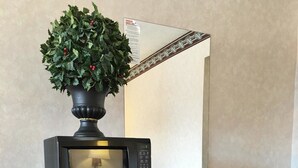 Ein kompakter, schwarzer Kühlschrank mit einer Mikrowelle obenauf, ein kleiner Holztisch und ein Blumentopf.