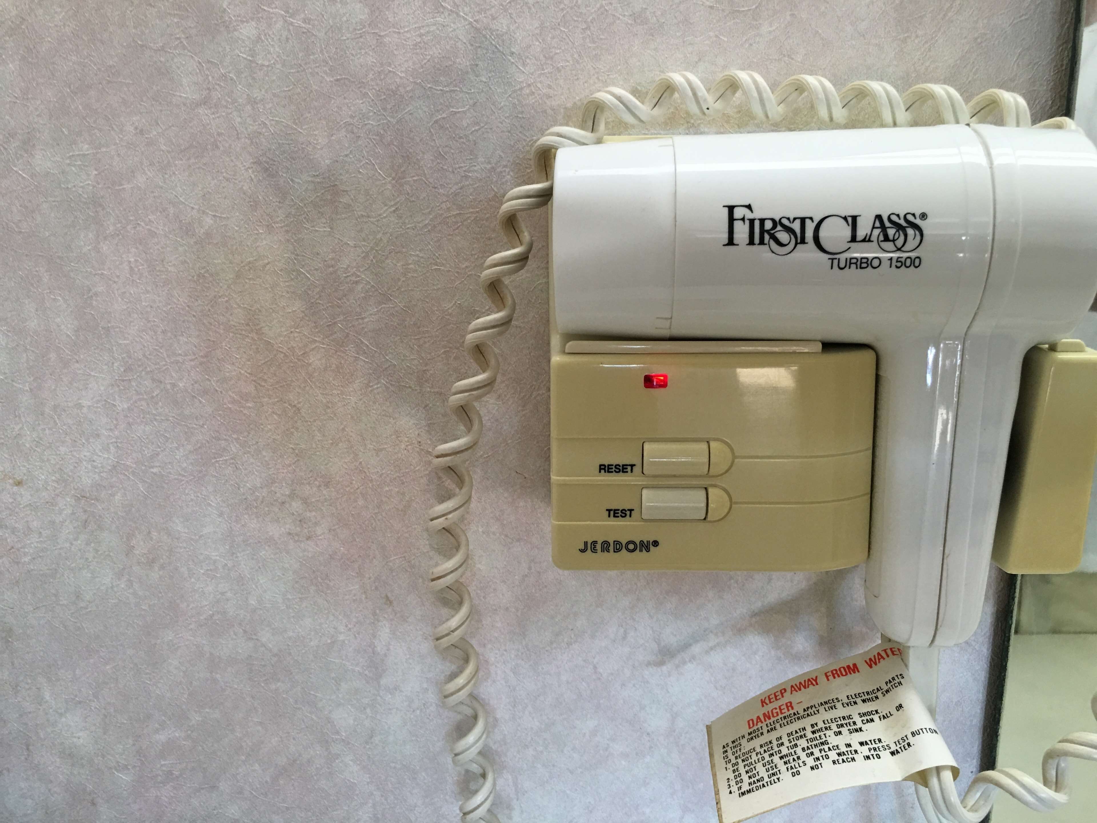 Secador de cabelo Turbo 1500 Classe Primeira, com painel de controle, incluindo botão RESET e TESTE, e etiqueta de advertência para manter longe da água.