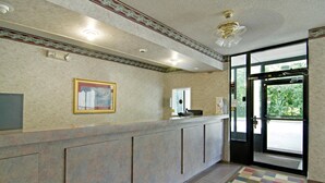 Ein Hotel-Empfangsbereich mit Empfangstresen, einem gerahmten Bild, einer Tür mit Zahlencode und einer blauen Fußmatte am Eingang.