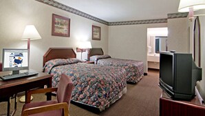 Ein Hotelzimmer mit zwei Betten, einem Schreibtisch mit Computer, einem Stuhl, einem Fernseher und zwei Lampen.