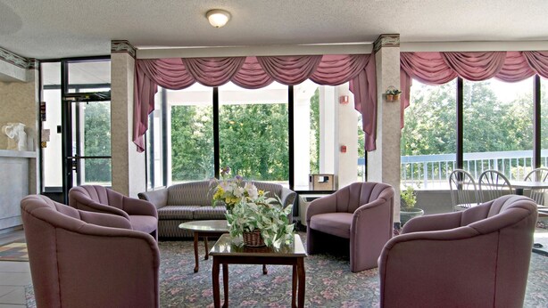 Ein geräumiger Wohnbereich mit einer Couch, Sesseln und einem Couchtisch. Große Fenster mit Vorhängen bieten einen Ausblick ins Freie.