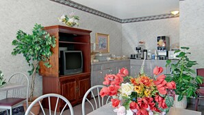 Ein Essbereich mit Tisch, Stühlen, einem Fernseher, einem Schrank und einer Blumenarrangement.