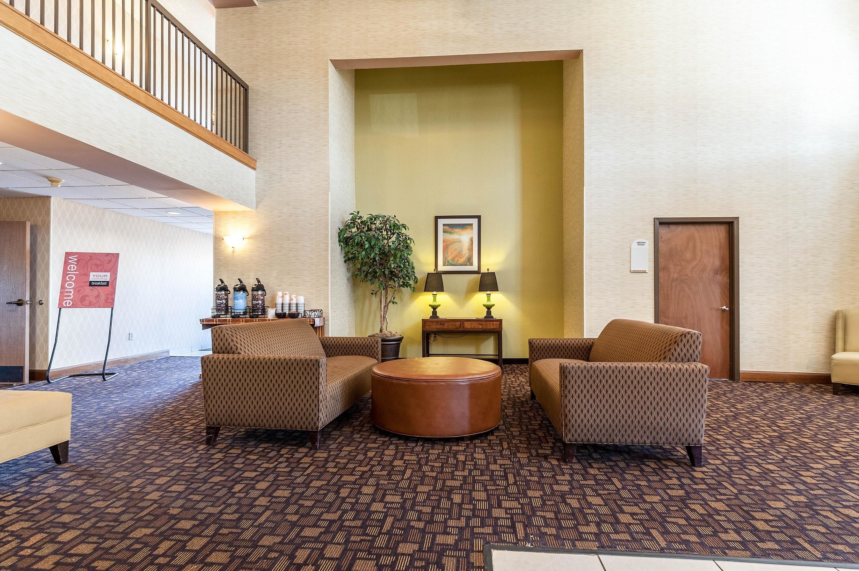 A lobby with patterned carpet, two sofas, a round coffee table, a plant, and a framed picture on the wall.