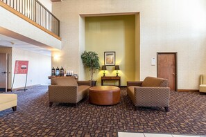 A lobby with patterned carpet, two sofas, a round coffee table, a plant, and a framed picture on the wall.