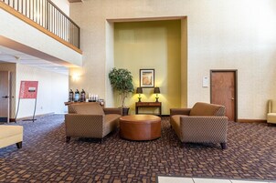 A lobby with patterned carpet, two sofas, a round coffee table, a plant, and a framed picture on the wall.