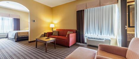 Een hotelkamer met een bed, een slaapbank, een salontafel en een stoel. Er is een raam met gordijnen en een airconditioning.
