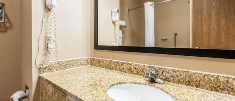 A bathroom with a granite countertop sink, a mirror, a hairdryer, and a towel rack.