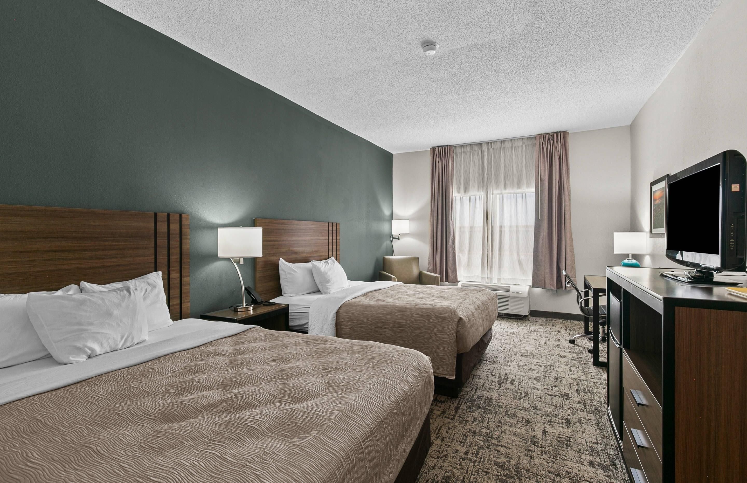 A hotel room with two beds, a desk with a television, and a window with curtains.