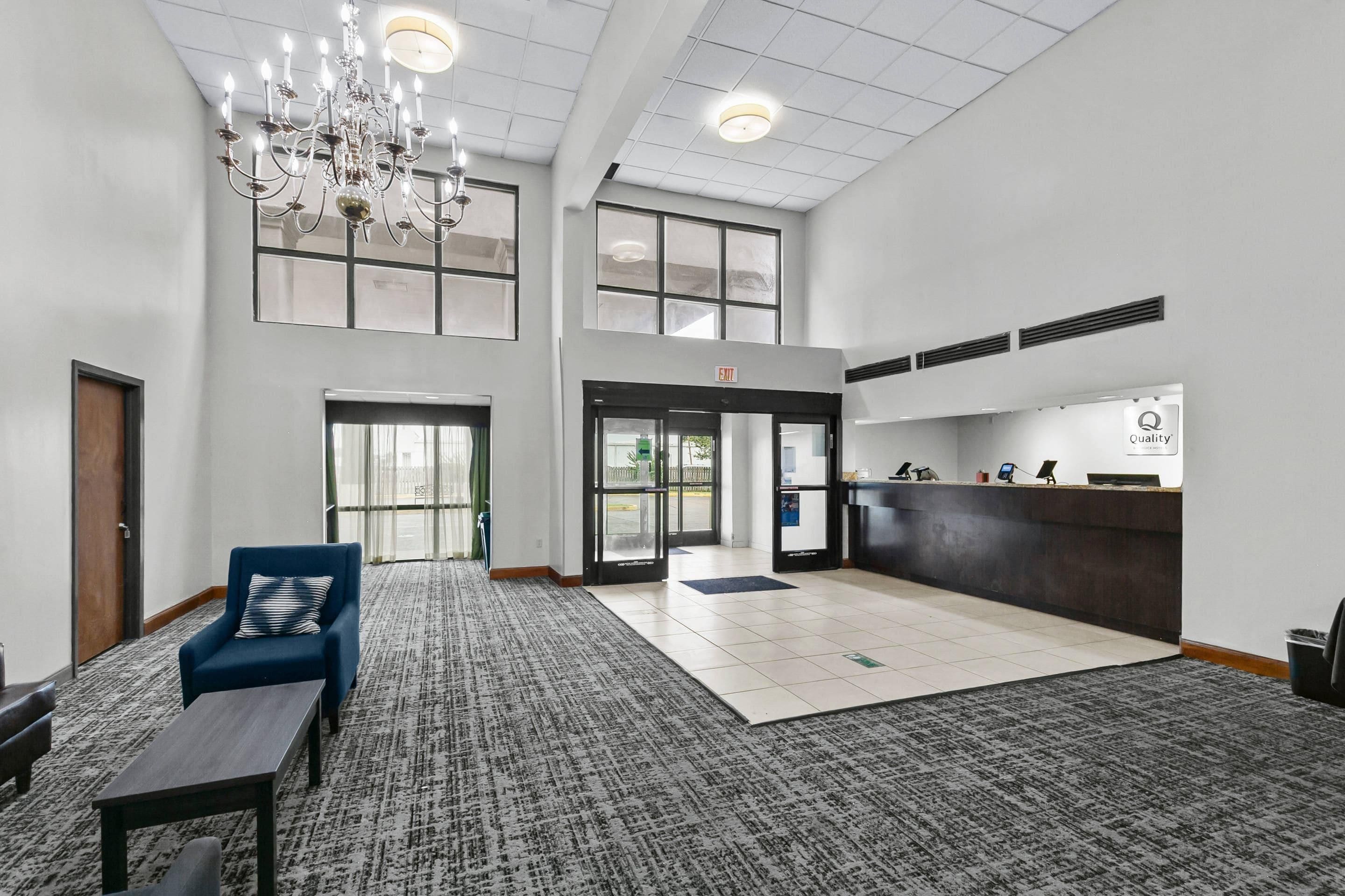 Eine geräumige Lobby mit einer Rezeption, einer Kristallleuchtre und einer Sitzecke mit blauem Sessel und kleinem Tisch.