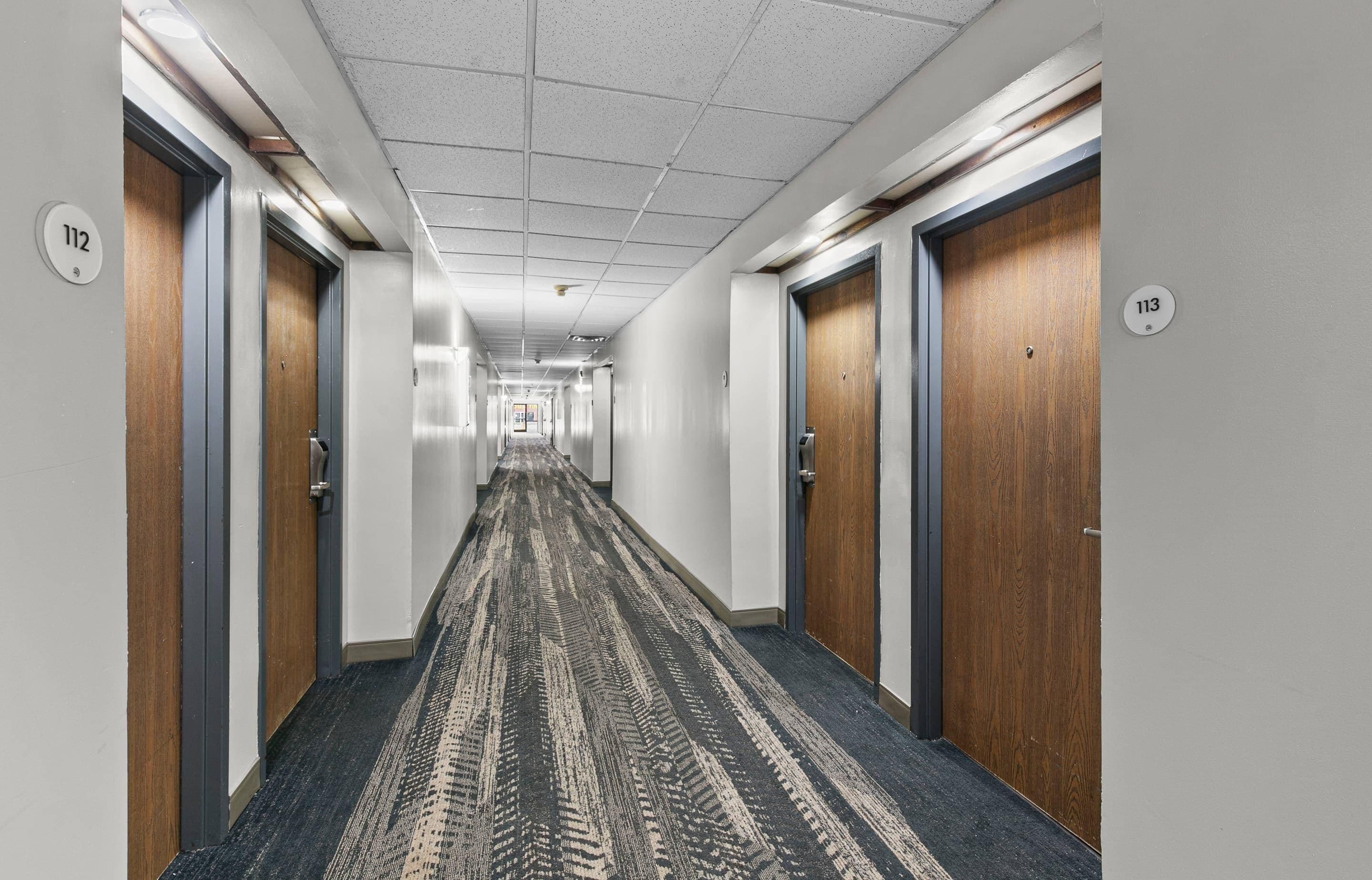 A hallway with doors numbered 112 and 113, carpeted floor, and a ceiling with recessed lighting.