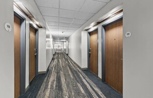 Un pasillo con puertas numeradas 112 y 113, suelo alfombrado e iluminación empotrada en el techo.
