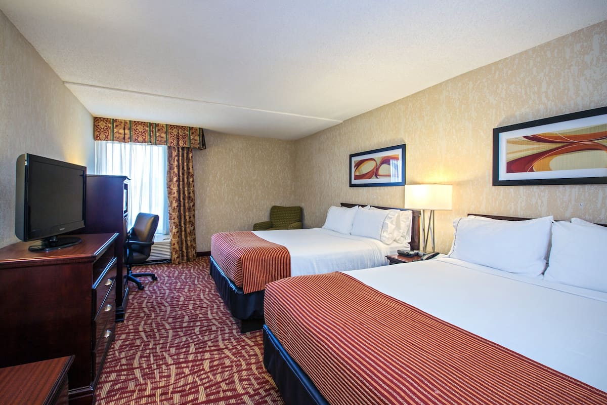 A hotel room with two beds, a desk with a television, a chair, and artwork on the walls.