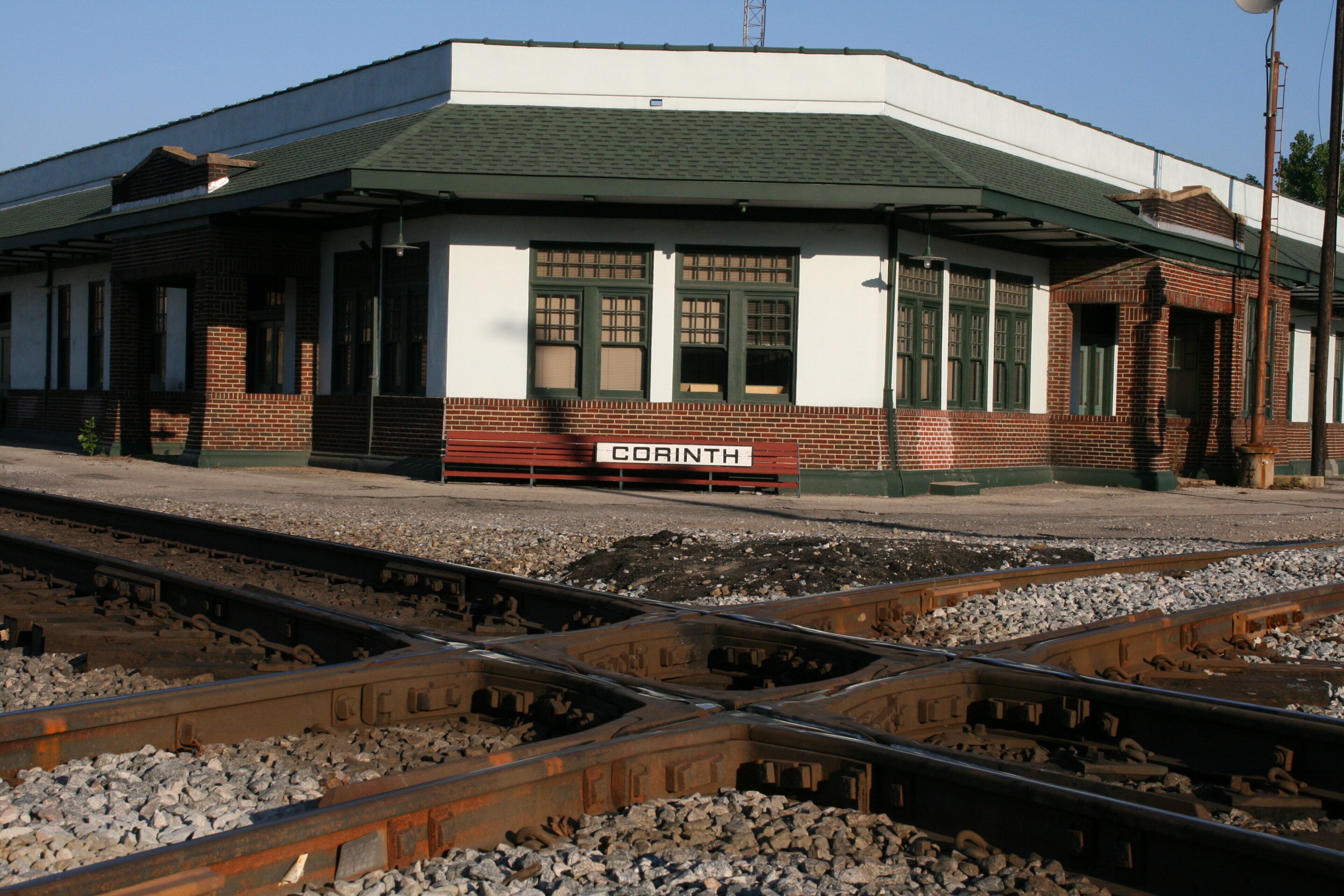 Andén de estación de tren con un cartel que dice 'CORINTH' y varias vías.