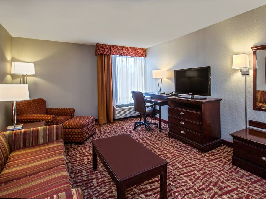 A hotel room with a sofa, a desk, a television, a dresser, and a patterned carpet.