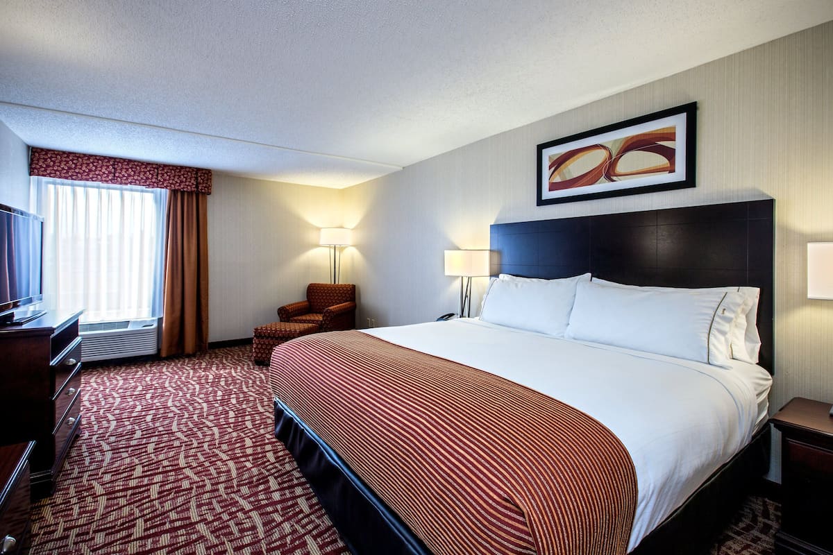 A hotel room with a large bed, a desk with a chair, a TV, and a window with curtains.