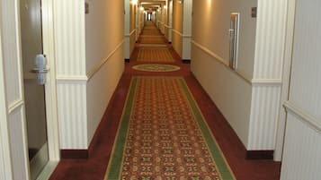 Een hotelgang met vloerbedekking, deuren aan weerszijden en een lamp aan de muur.
