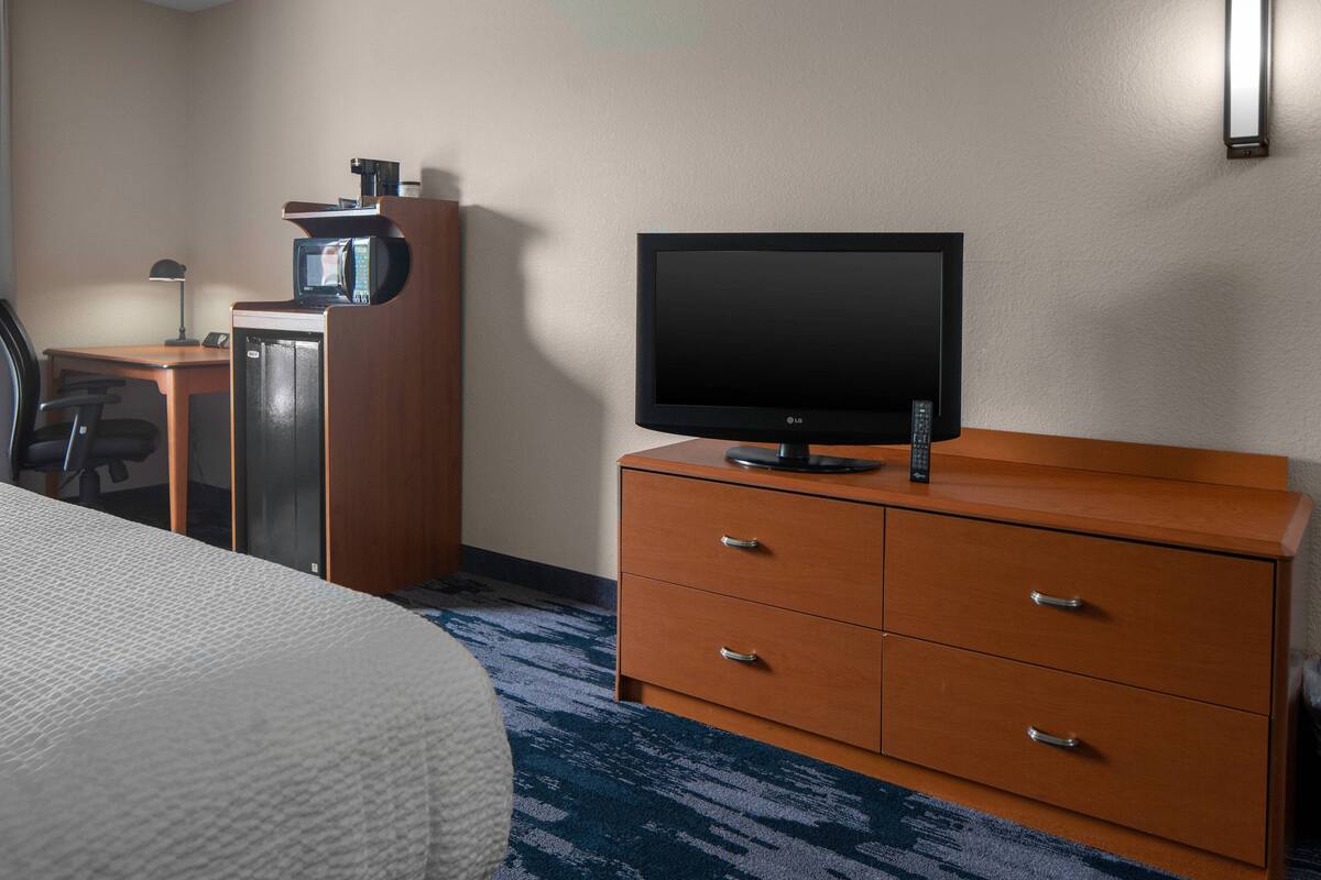 Ein Hotelzimmer mit einem Bett, einem Fernseher auf einer Holzkombie, einer Mikrowelle und einem Schreibtisch mit Lampe.