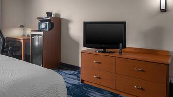 A hotel room with a bed, a TV on a wooden dresser, a microwave, and a desk with a lamp.