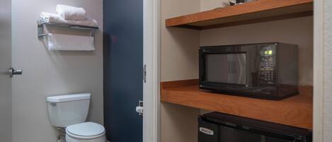 A compact bathroom with a toilet, a microwave, and a refrigerator.