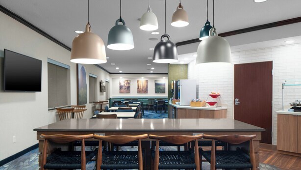 A modern dining area with a large table and chairs, multiple pendant lights, and a kitchen area in the background. - Fairfield Inn & Suites by Marriott - Jefferson City (Jefferson City)