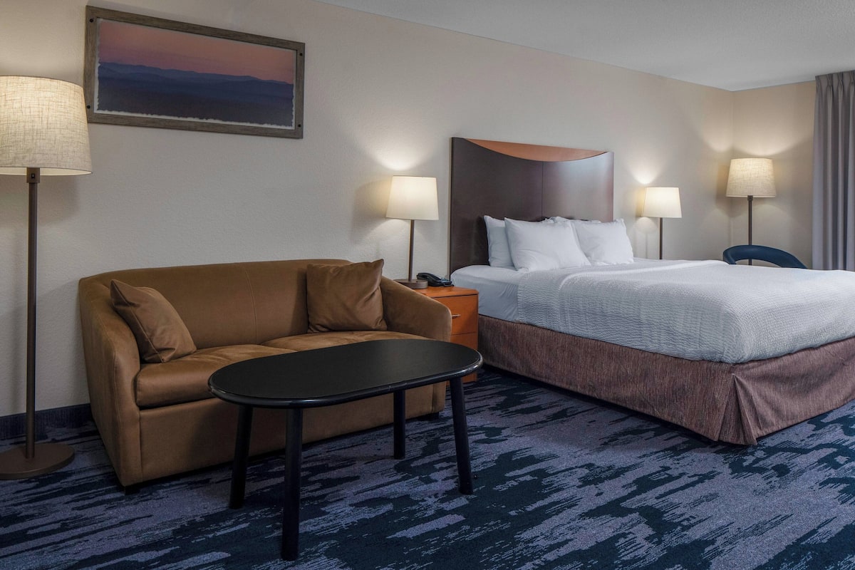 Ein Hotelzimmer mit einem braunen Sofa, einem kleinen runden Tisch, einem Bett mit weißer Bettwäsche, zwei Nachttischlampen und einem Bild an der Wand.