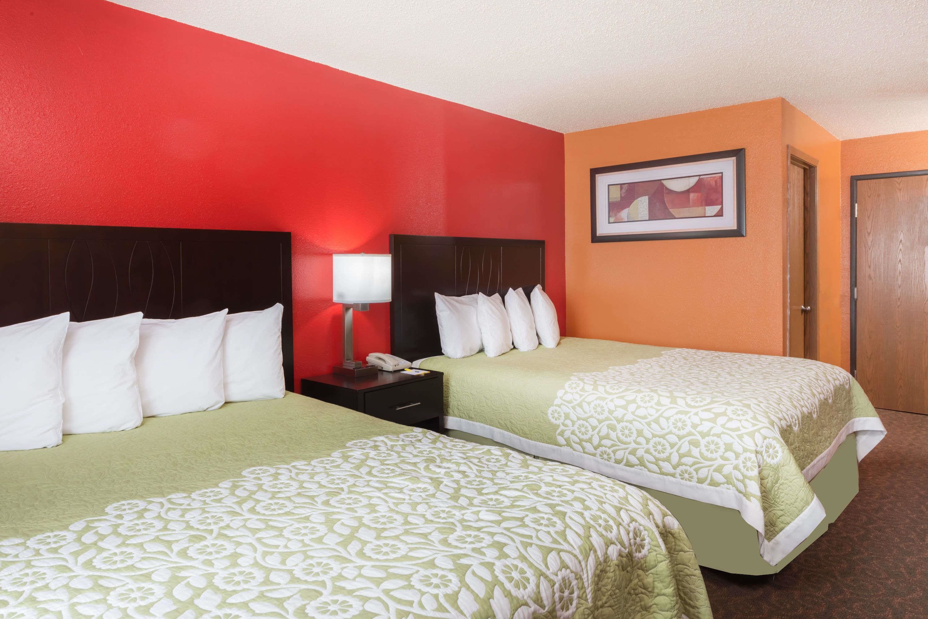 A hotel room with two beds, a nightstand with a lamp, and a framed picture on the wall.