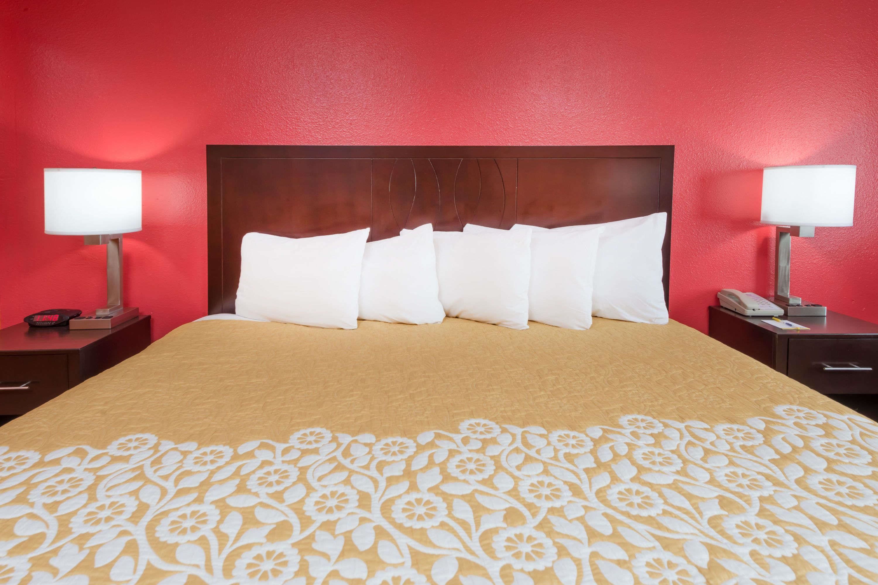 Habitación de hotel con una cama grande, paredes rojas y dos mesitas de noche con lámparas.