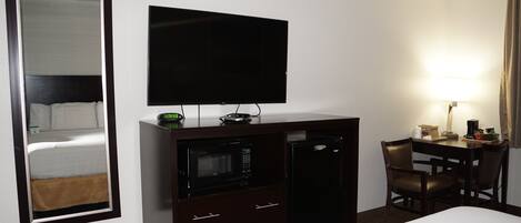 A hotel room with a bed, a TV, a microwave, a desk with a chair, and a lamp.