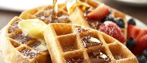 Un plato de waffles con almíbar, mantequilla y bayas frescas.