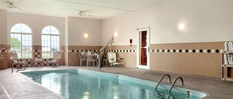 Una piscina interior con indicador de profundidad de 1.5 metros, rodeada de sillas de descanso y una pared de azulejos con diseño de diamantes.