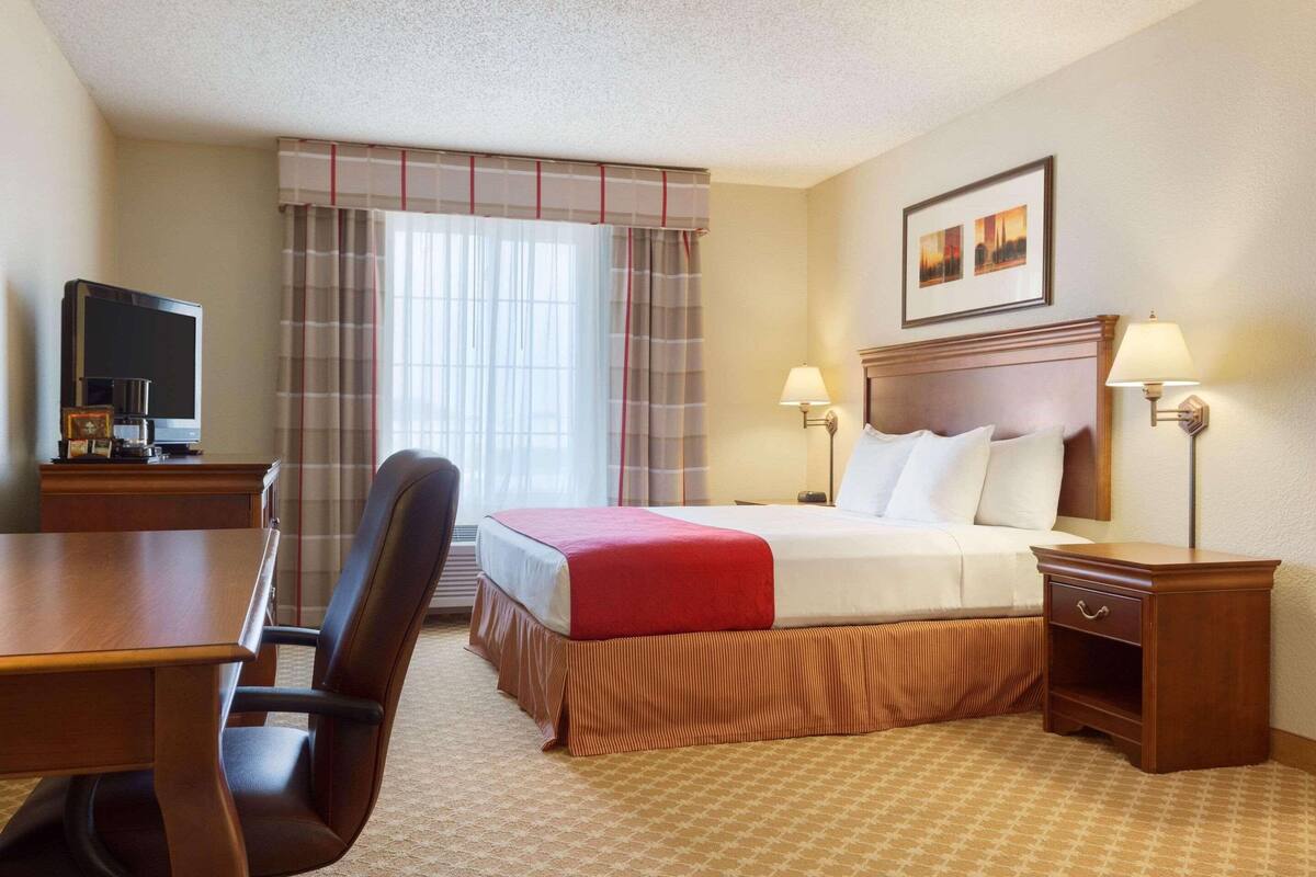 A hotel room with a bed, bedside tables, a desk, a chair, and a television.