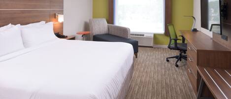 A hotel room with a large bed, a desk, a chair, a TV, and a window.