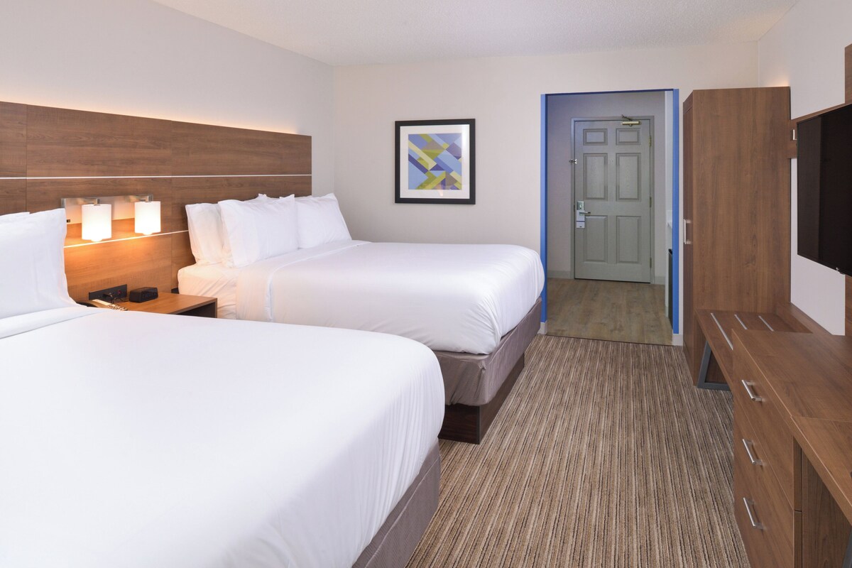 A hotel room with two beds, a bedside table with lamps, a framed picture on the wall, a door, and a wardrobe.
