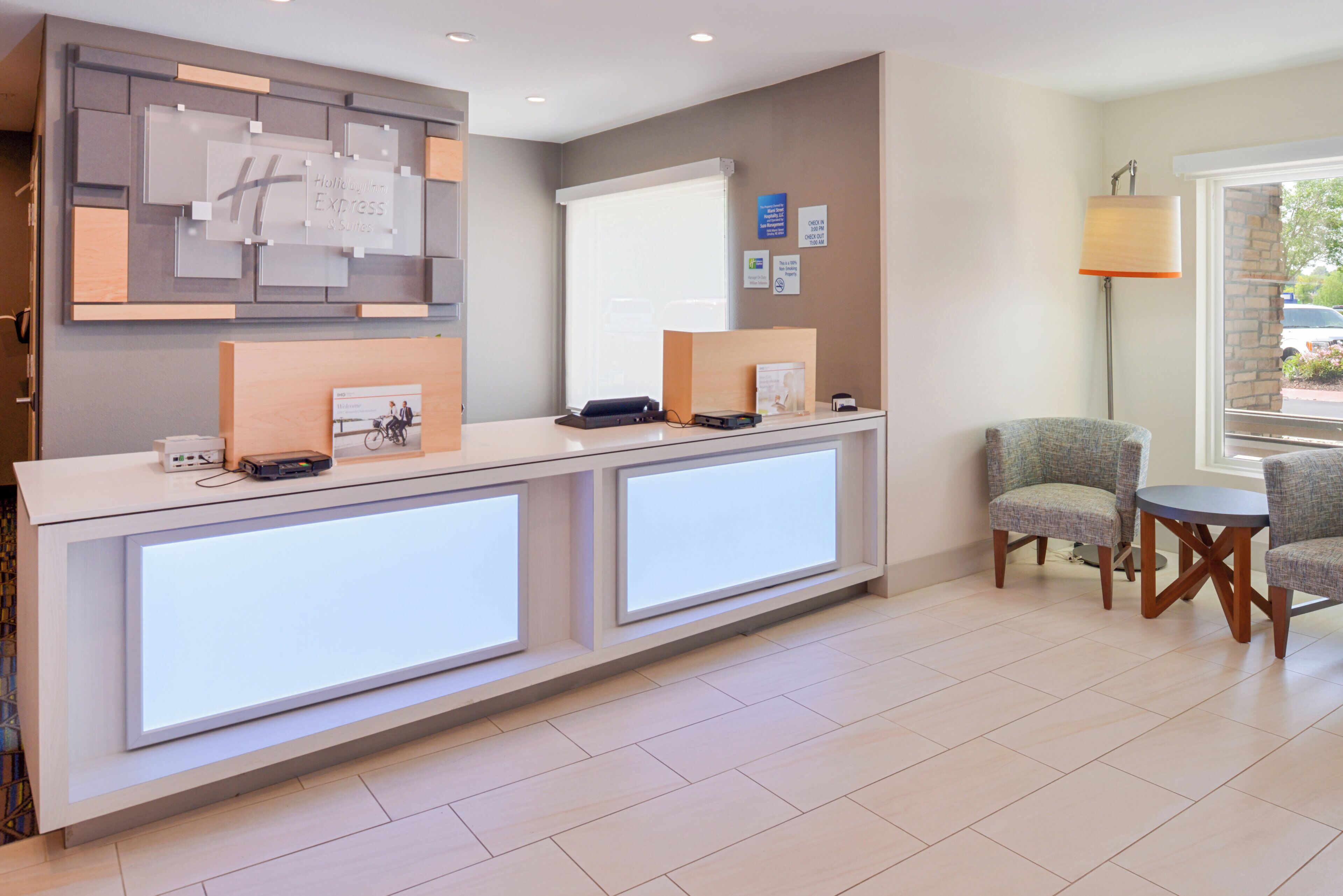 A reception desk with a digital display, a bulletin board, and a seating area with two chairs.