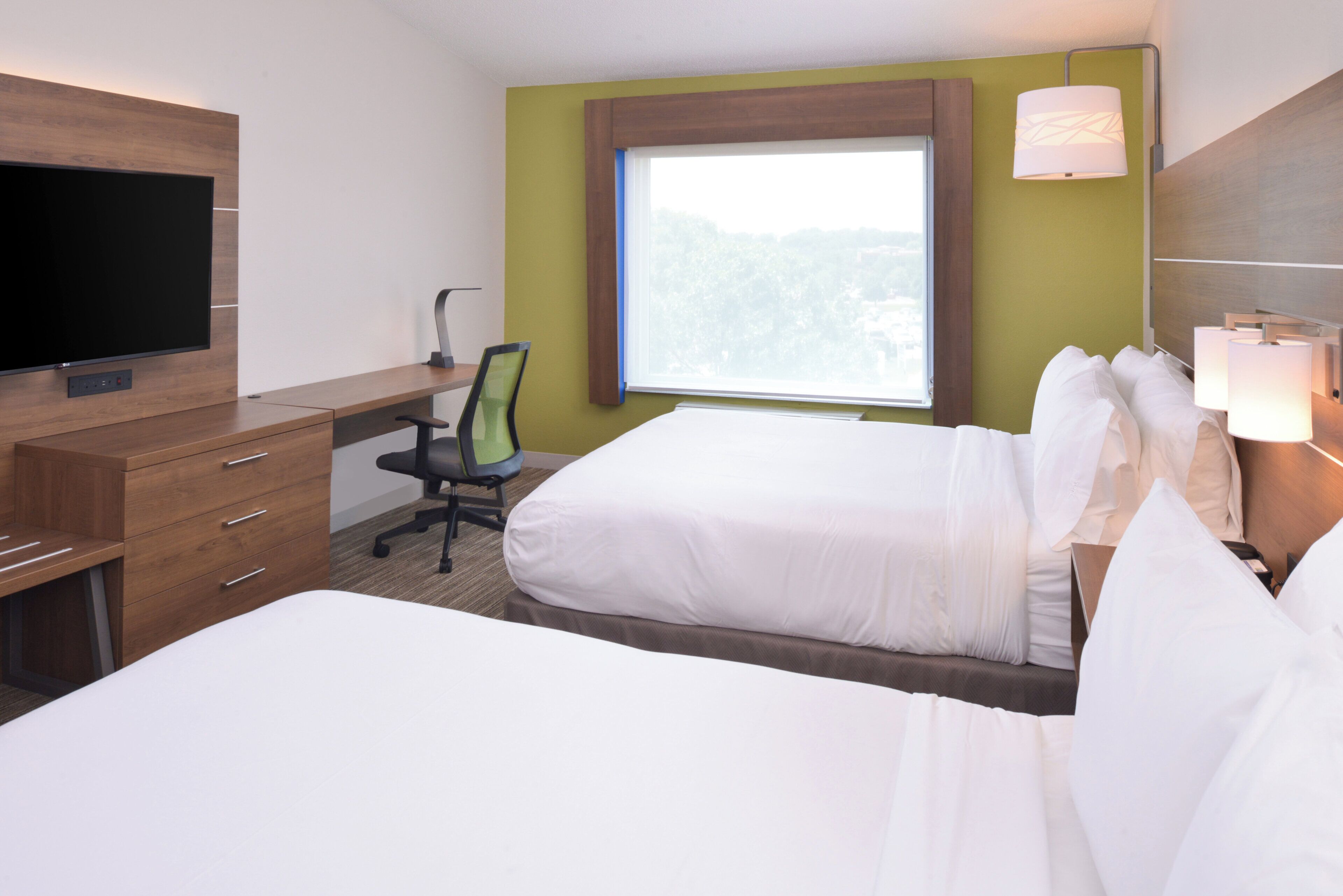A hotel room with a bed, a desk with a chair, a television, and a window with a view.