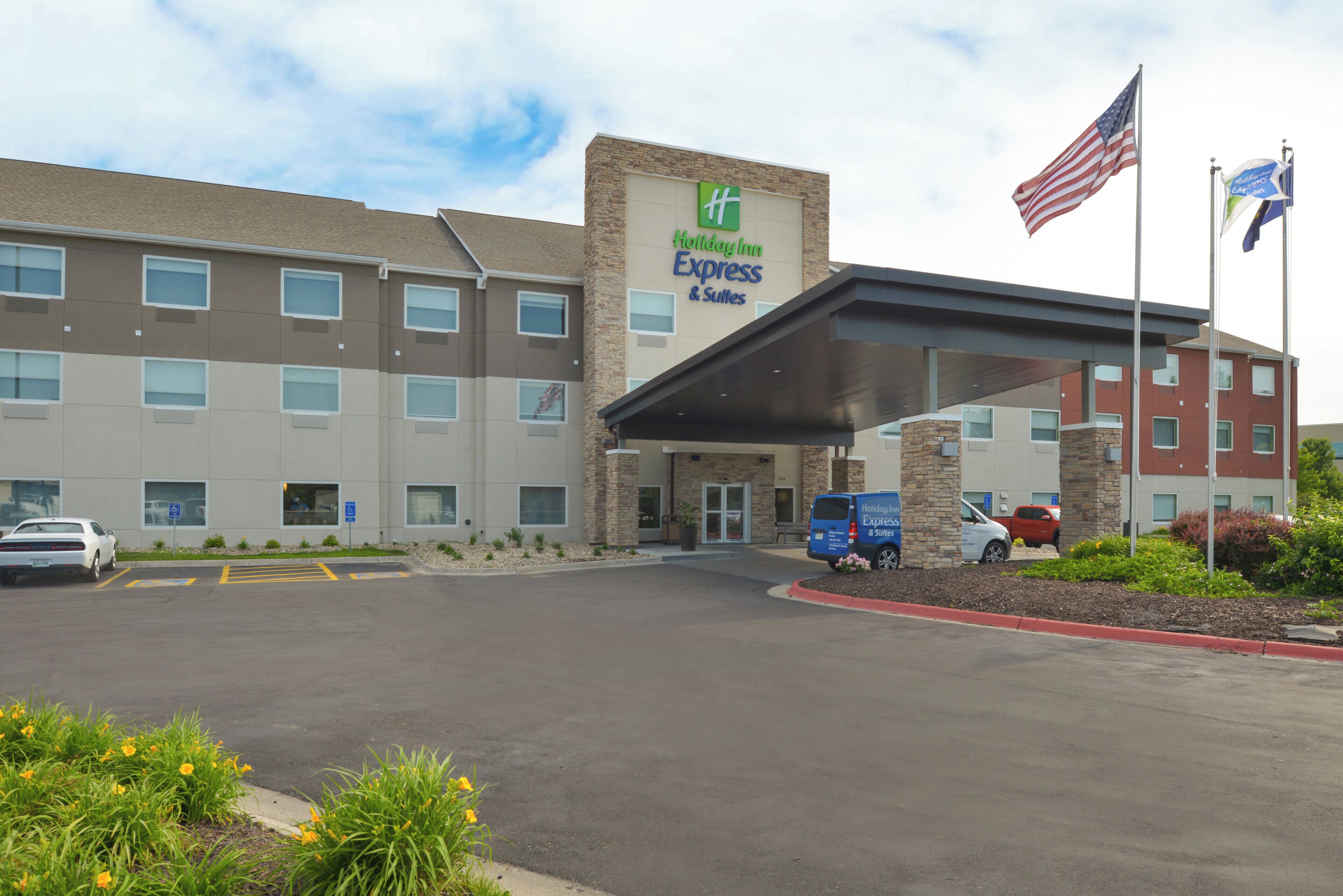 Edificio de Holiday Inn Express & Suites con entrada cubierta, estacionamiento y banderas estadounidenses.